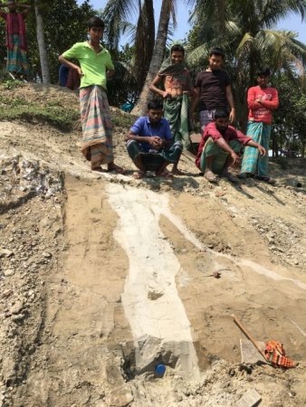 A group of people stand atop a steep slope of dirt that has a light colored strip running down it